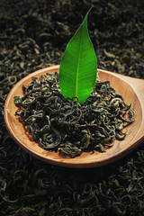 Pile of dry tea with wooden spoon and green leaf, close up