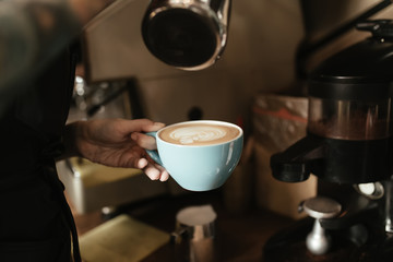 Barista woman holding cup of coffee with milk foam