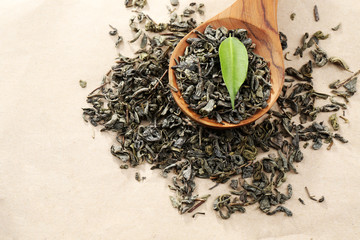 Scattered tea with green leaves in wooden spoon on burlap background