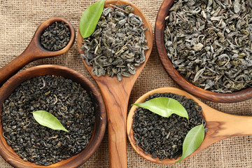 Dry tea with green leaves in wooden spoons on burlap background