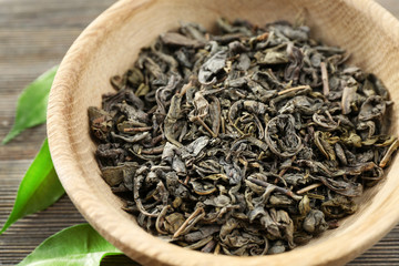 Dry tea with green leaves in bowl on wooden table background