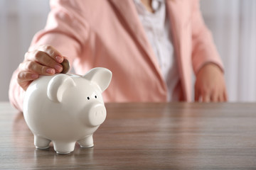 Obraz na płótnie Canvas Woman putting coin into piggy bank at the table