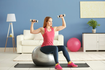 Fototapeta na wymiar Young sportswoman doing exercises with ball and dumbbells on a mat at home