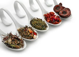Different sorts of dry tea in ceramic spoons, isolated on white