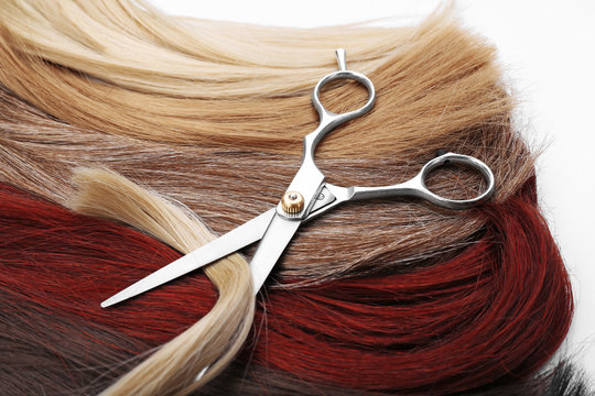 Hairdresser's scissors with varicolored strands of hair on background