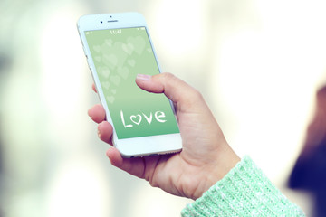 Female hand holding a mobile phone with romantic screensaver, outdoors