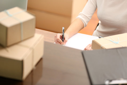 Delivery concept. Woman signs papers among parcels, close up