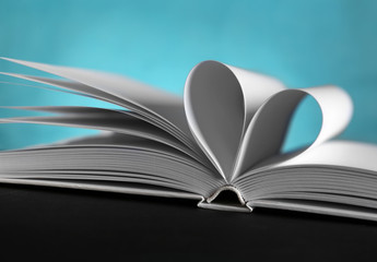 Sheets of book curved into heart shape on unfocused blue background