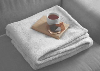 A soft blanket, a books, a cup of tea and a piece of chocolate on the sofa. Peace and comfort concept
