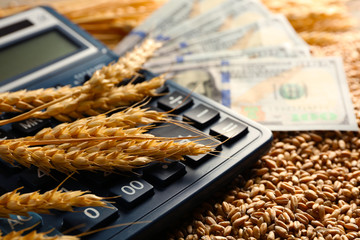 Dollar banknotes, calculator and wheat grains on wooden background. Agricultural income concept