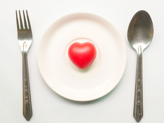 Red heart on plate with fork and spoon on white background.