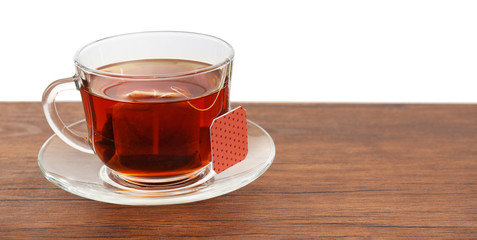 Glass cup with tea bag on wooden table over white background