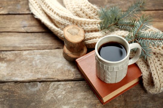 Cup of hot drink with knitted warm winter scarf on old wooden table