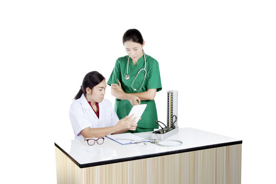 Two Asian Female Doctor Using Tablet Computer Reviewing Medical Chart, Isolated On White