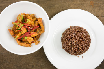 The delicious homemade Thai paneang curry food (pork peanut coconut cream curry or panang curry with pork) and cooked dark brown rice on the white plate on old wooden planks for good healthy.