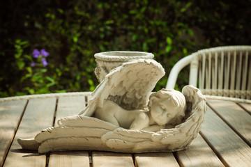 sleeping angel (cupid) statue on wood table and chair in the gar