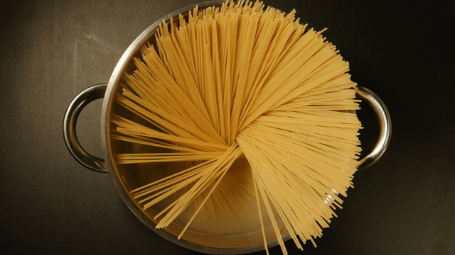 TOP VIEW: A cook puts down a spaghetti in a steel pot (round)
