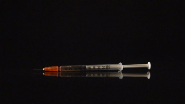 SLOW: A medical syringe falls on a black desk
