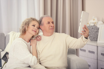 Happy mature couple taking photo of their self with tablet together at home