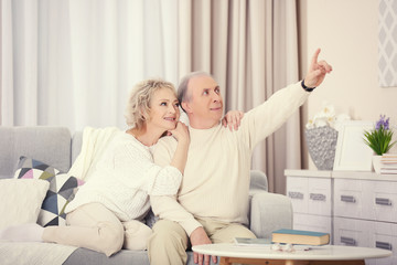 Surprised happy mature couple sitting on a sofa and looking towards together at home