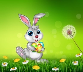 Happy little bunny holding easter eggs on grass background 