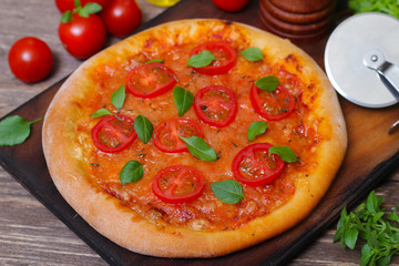 Italian cuisine. Mediterranean cuisine. Pizza Margherita with tomato topped with melted golden cheese, herbs and basil served  on old wooden table