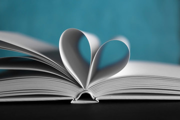 Sheets of book curved into heart shape on unfocused blue background