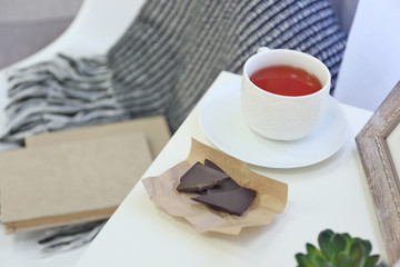 A cup of tea, chocolate, books and blanket in the room
