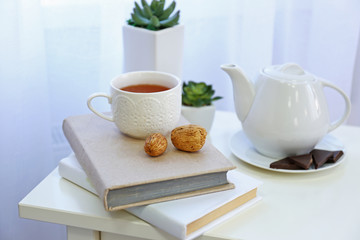 Books, a teapot, a cup of tea and nuts on the table in the room
