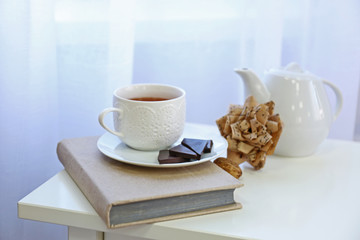 A cup of tea, chocolate, book and handmade paper flower on the table in the room