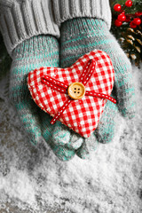 Female hands in blue mittens with decorative heart on snow background