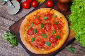 Italian cuisine. Mediterranean cuisine. Pizza Margherita with tomato topped with melted golden cheese, herbs and basil served  on old wooden table