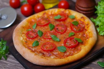 Italian cuisine. Mediterranean cuisine. Pizza Margherita with tomato topped with melted golden cheese, herbs and basil served  on old wooden table