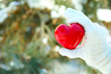 Fototapeta premium Woman hand in knitted mitten holding red heart on winter background
