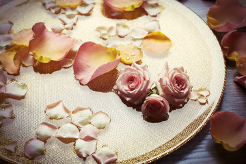 Pink and yellow rose petals in golden bowl with water on wooden background