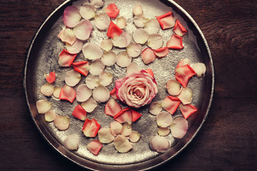 Pink and white rose petals in silver bowl on wooden background