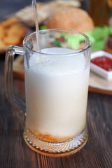 Glass mug of draft light beer with snacks on dark wooden table, close up