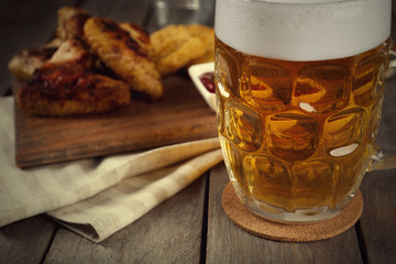 Glass of beer and chicken wings on wooden table, close up