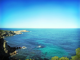 Rocky coastline background and clear blue and turquoise sea with copy space.