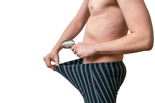Impotence concept. Man with magnifying glass is looking inside boxers on his small penis. Isolated on white background.