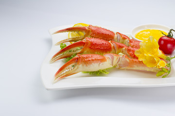 Boiled crab claws with sauce and lemon on a plate over white background