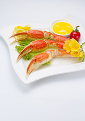 Boiled crab claws with sauce and lemon on a plate over white background