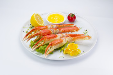 Boiled crab claws with sauce and lemon on a plate over white background