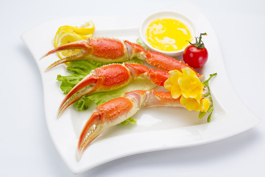 Boiled crab claws with sauce and lemon on a plate over white background