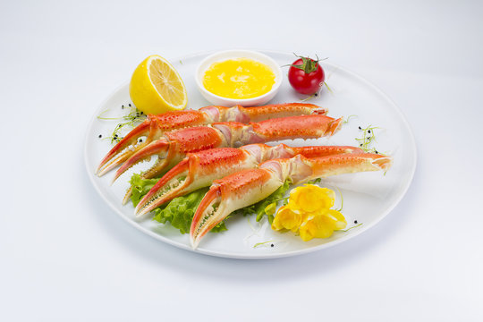 Boiled crab claws with sauce and lemon on a plate over white background