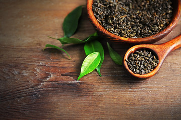 Granulated tea with green leaves in wooden bowl on table closeup