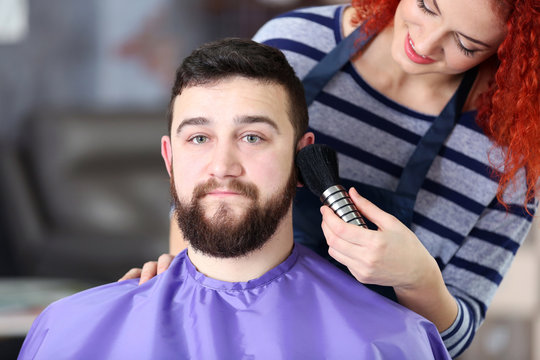 Professional hairdresser cleaning handsome client face with brush