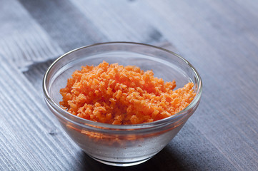 Fototapeta na wymiar Minced carrots in a glass bowl on a wood background