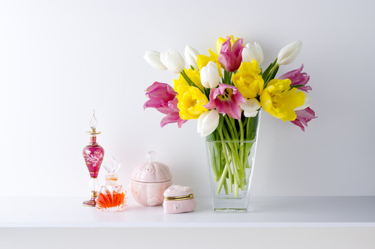白い背景と棚と花瓶と3色のチューリップと器と香水瓶