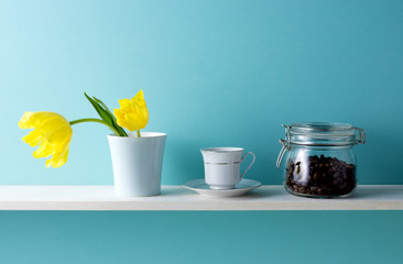 青い背景と棚と黄色いチューリップとコーヒーカップとコーヒー豆